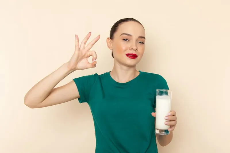 Woman holding a glass of milk and gesturing OK sign, illustrating the question is milk good for dry eyes.