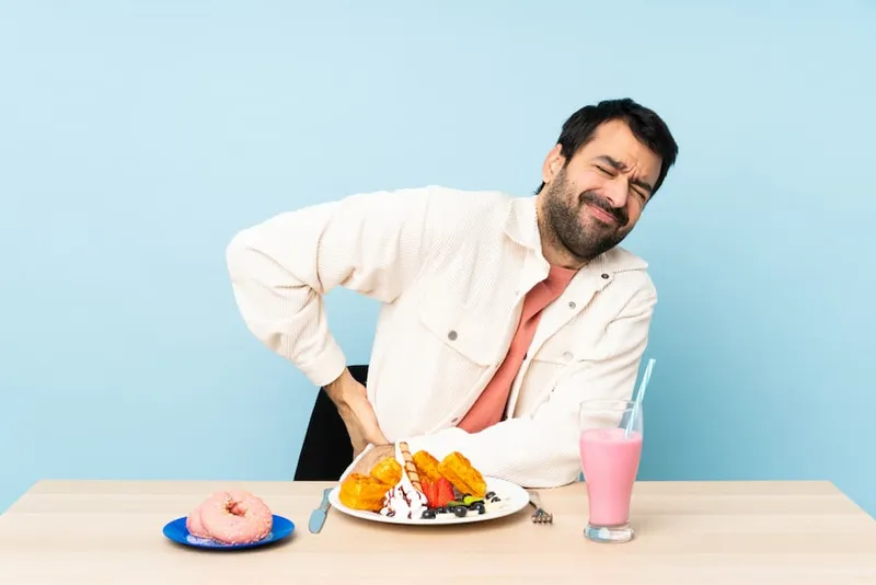 Man experiencing kidney stone discomfort while eating unhealthy foods, illustrating What to eat and What to avoid for kidney stone prevention