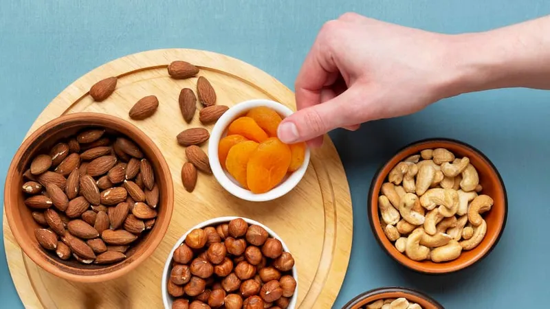Which dry fruit is good for fatty liver? A top view of almonds, cashews, hazelnuts and dried apricots arranged in bowls with a hand picking one