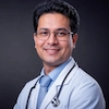 Confident Indian male doctor in white coat with stethoscope offering medical consultation